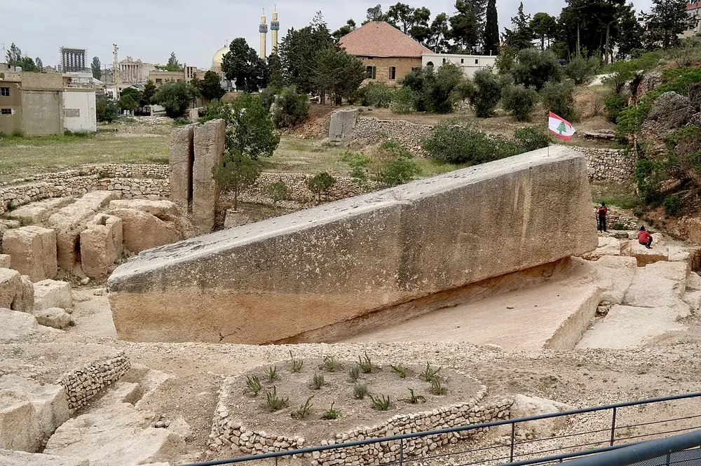 A vast rectangular stone block lying tilted in an ancient quarry, with people standing on it for scale
