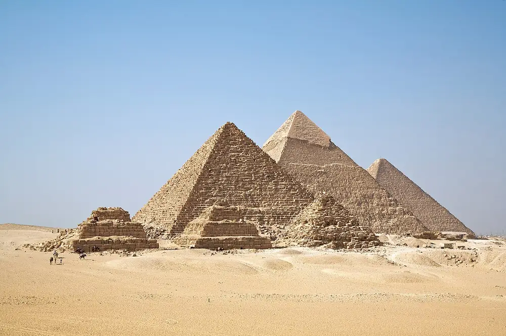 The three pyramids of Giza standing in desert under a pale sky