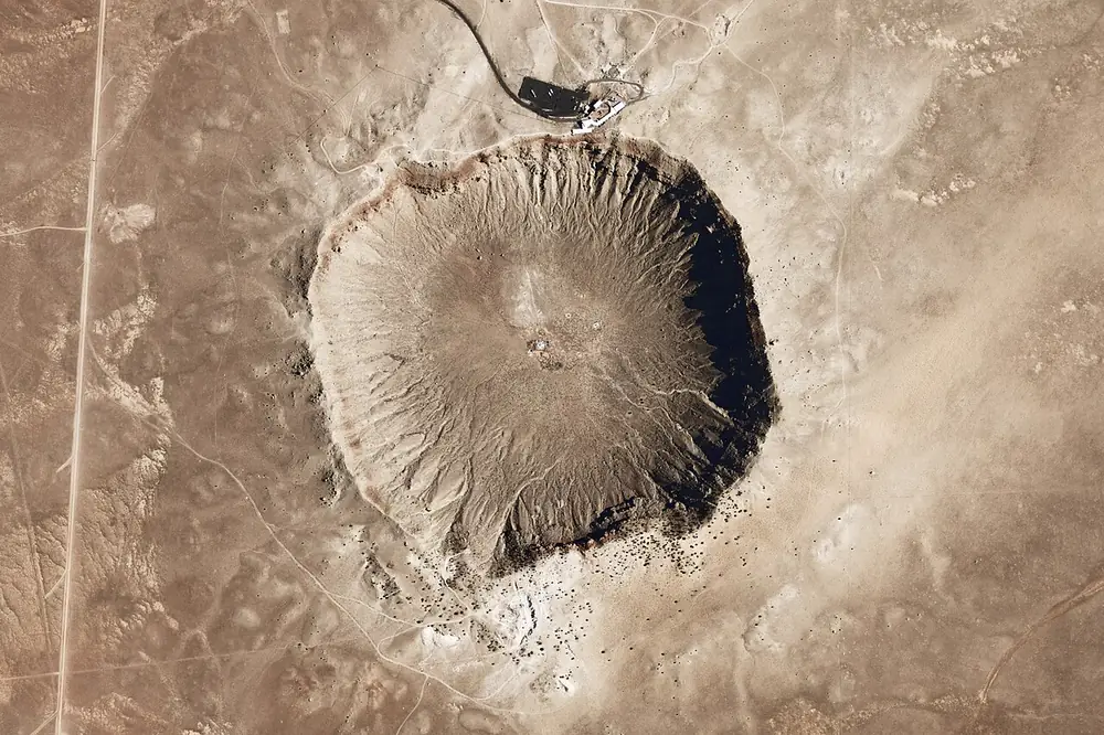 A large round crater with raised rims in flat desert, seen from above